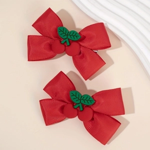 Close-up of red ribbon hair clips with cherry charms on a minimalist beige background