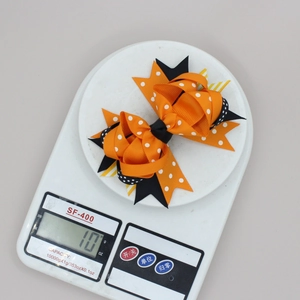 Détail d'une pince à cheveux multicouche orange à pois pesant 10g sur une balance