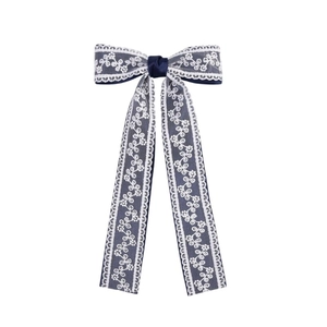 Detail of navy blue satin hair clip with white floral lace layers and long streamers