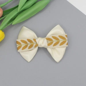 Elegante fermaglio per capelli in raso crema con ricamo di foglie dorate su fondo grigio