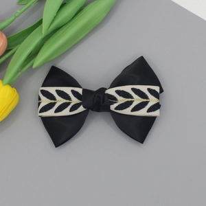 Elegante fiocco per capelli nero con motivo a foglie e filo dorato su sfondo grigio