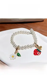 Détail d'un bracelet en perles avec breloques fraise, fleur et feuille sur un plateau