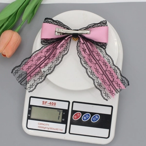Pink satin bow hair clip with black lace trim weighing 7g on a digital scale