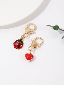 Détail de pendentifs coccinelle et cœur avec fermoirs mousquetons dorés sur fond blanc