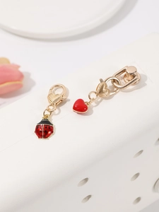 Détail de pendentifs coccinelle et cœur avec fermoirs mousquetons dorés sur support