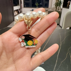 Handheld view of a graduation pearl bracelet with a gold heart clasp and graduate charm