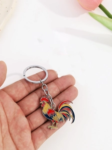 Close-up of vibrant enamel rooster keychain with polished metal ring held in hand