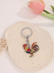 Close-up of colorful enamel rooster keychain on a decorative ceramic display plate
