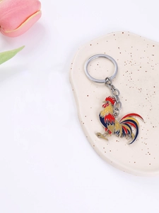 Colorful rooster metal keychain with enamel finish displayed on a ceramic tray with tulip