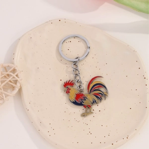 Exquisite rooster metal keychain with vibrant enamel colors on a beige ceramic tray