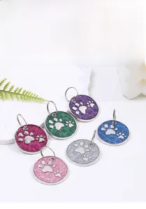 Detail of colorful glitter dog ID tags with paw prints on a white stone background