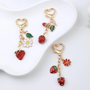 Charming strawberry metal keychain with heart clasp and floral charms on a white plate