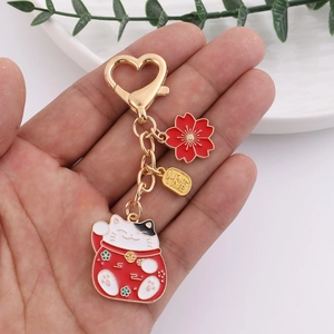 Lucky cat metal keychain with red flower, gold tag, and heart-shaped hook in hand