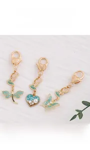 Detail of dragonfly and butterfly charms with green enamel and pearls on gold keychains