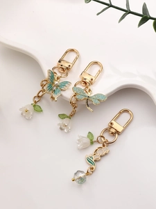 Detail view of gold metal keychains with green enamel butterfly and dragonfly motifs