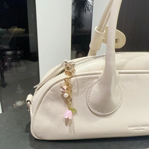 Detail of pink tulip and butterfly bag charm attached to a white leather handbag