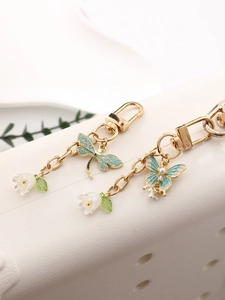 Detail of dragonfly and butterfly charms with lily of the valley on gold keychains