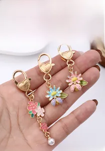 Détail de fermoirs cœur dorés avec breloques fleurs en émail et abeilles sur porte-clés