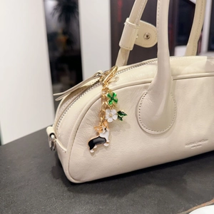 Golden Corgi keychain with white flower and green clover charms on a beige handbag