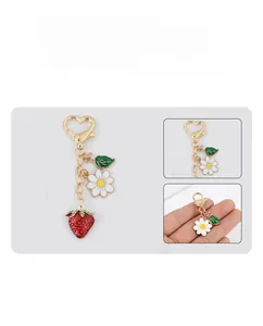 Detail of metal keychain with strawberry and daisy charms plus golden heart-shaped clasp