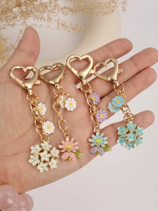 Detail showing hand holding enamel flower and bee keychains with heart-shaped clips