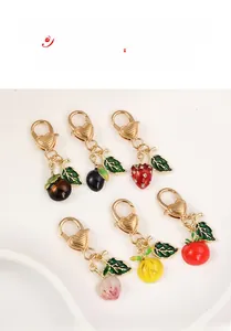 Detailed close-up of six assorted enamel fruit and vegetable keychains with gold metal finish