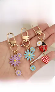 Detail of colorful enamel daisy and ladybug charms on a light gold lobster clasp keychain