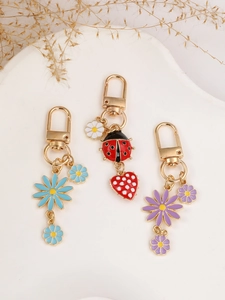 Detail of colorful daisy and ladybug keychains with golden lobster clasps on a white pedestal