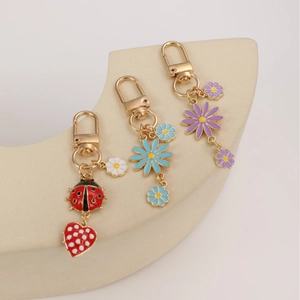 Daisy and ladybug keychain charms with gold metal hardware on geometric display