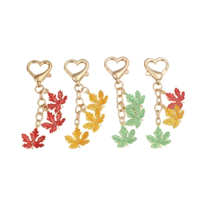 Set of four colorful maple leaf keychains with golden heart clasps on white background