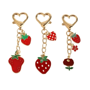 Three gold metal strawberry enamel keychains with heart hooks on a plain white background