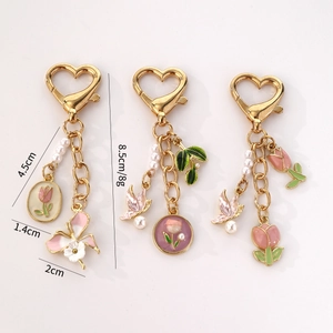 Trois porte-clés cœur dorés avec fleurs émaillées et perles sur un fond blanc neutre