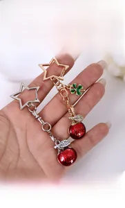 Close-up of red apple and green clover charms on star-shaped metal keychains held in hand