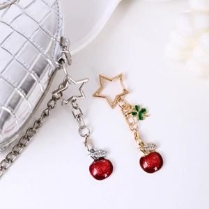 Red apple keychain with star-shaped clasp and leaf charms on a white leather bag