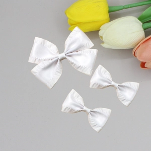 Detail of white pleated satin bow hair clips with delicate textured edges and soft silk luster