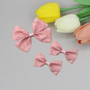 Close-up of three pink satin bow hair clips with elegant pleated edges on a grey surface