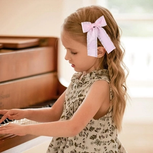 Pink satin bow hair clip with ruffle edges on a young girl at a piano setting