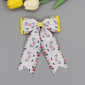 Detail of white bow hair clip with unicorn and floral prints and yellow grosgrain ribbon