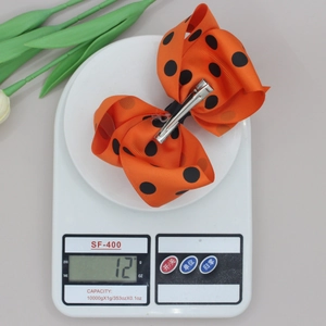 Détail d'une pince à cheveux orange à pois montrant un poids de 12g sur une balance