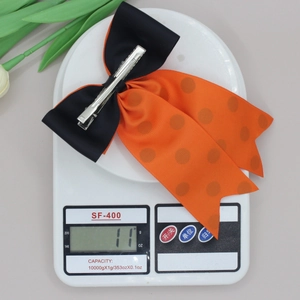 Détail d'une pince à cheveux à nœud orange à pois sur une balance pesant 11g