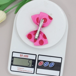 Lichtgewicht roze haarspeld met polkadot strik en metalen clip op een weegschaal