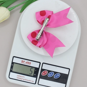Roze haarstrik met rode stippen op een weegschaal die het gewicht van 5g toont
