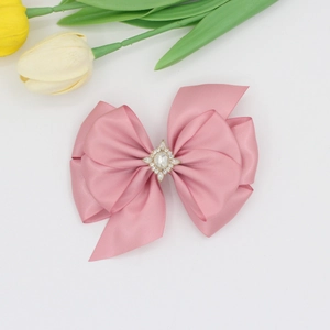 Détail de la pince à cheveux noeud en satin rose avec centre en strass étincelant