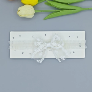 Détail d'un bandeau bébé en dentelle blanche avec nœud papillon et motifs floraux