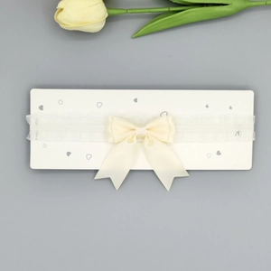 Détail du bandeau à nœud en satin crème avec bande élastique à volants sur carton blanc