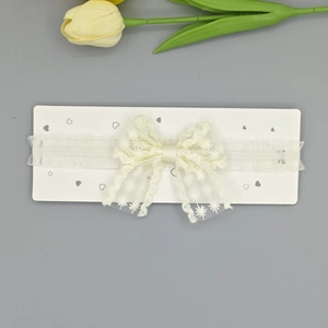 Gros plan d'un bandeau bébé en dentelle crème avec broderie marguerite sur une carte