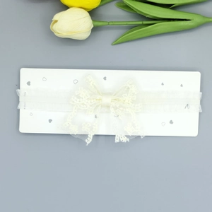 Détail d'un bandeau en dentelle blanche pour bébé avec un grand nœud sur carte cœur