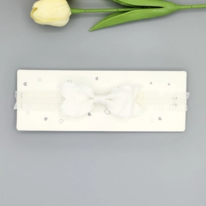 Détail d'un bandeau blanc en dentelle pour bébé avec nœud et bande élastique sur carte