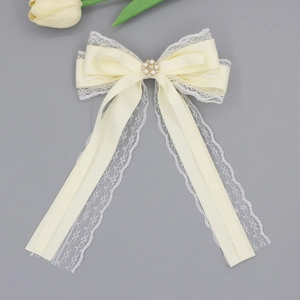 Detail of cream lace bow hair clip with pearl center and elegant hanging ribbons
