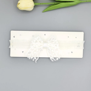 Détail d'un bandeau en dentelle blanche avec nœud à pois sur carte de présentation